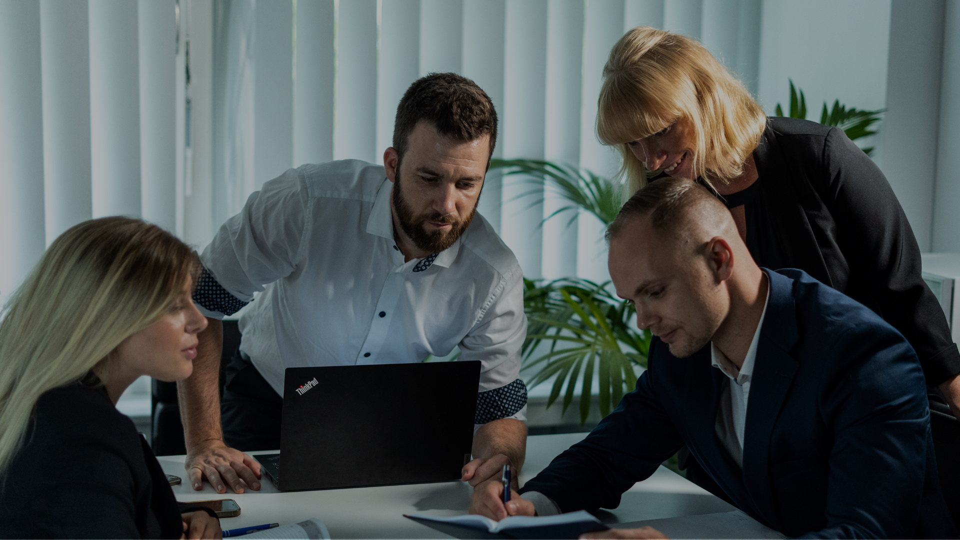 Ein Team aus zwei Männern und zwei Frauen sitzt gemeinsam an einem Tisch und arbeitet an einem Projekt.